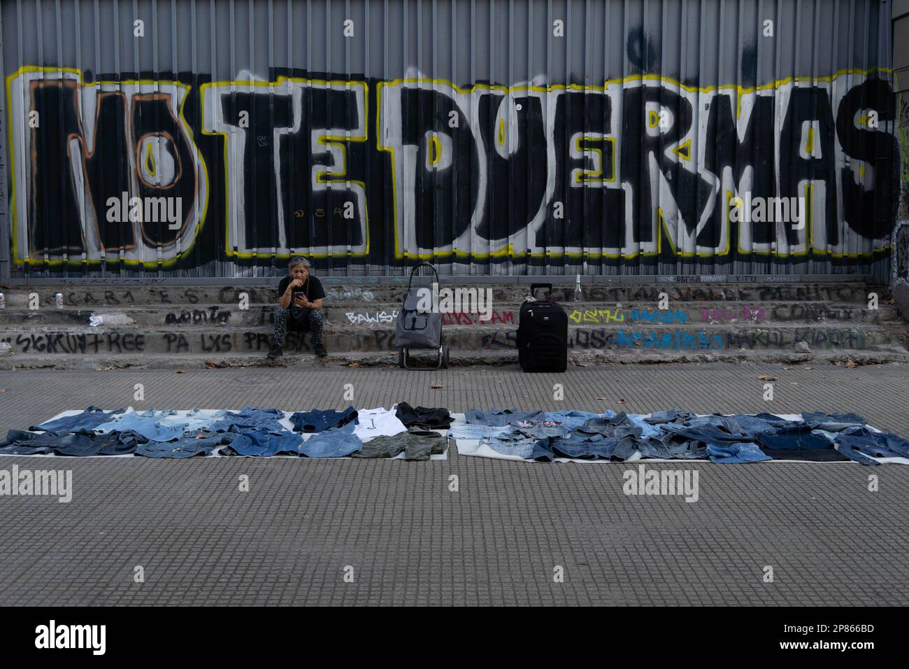 Santiago, Metropolitana, Chile. 8. März 2023. Eine Frau verkauft auf der Straße Kleidung vor einem Wandgemälde mit dem Satz „nicht einschlafen“, während eines märz anlässlich des Internationalen Frauentags in Santiago, Chile. (Kreditbild: © Matias Basualdo/ZUMA Press Wire) NUR REDAKTIONELLE VERWENDUNG! Nicht für den kommerziellen GEBRAUCH! Kredit: ZUMA Press, Inc./Alamy Live News Stockfoto