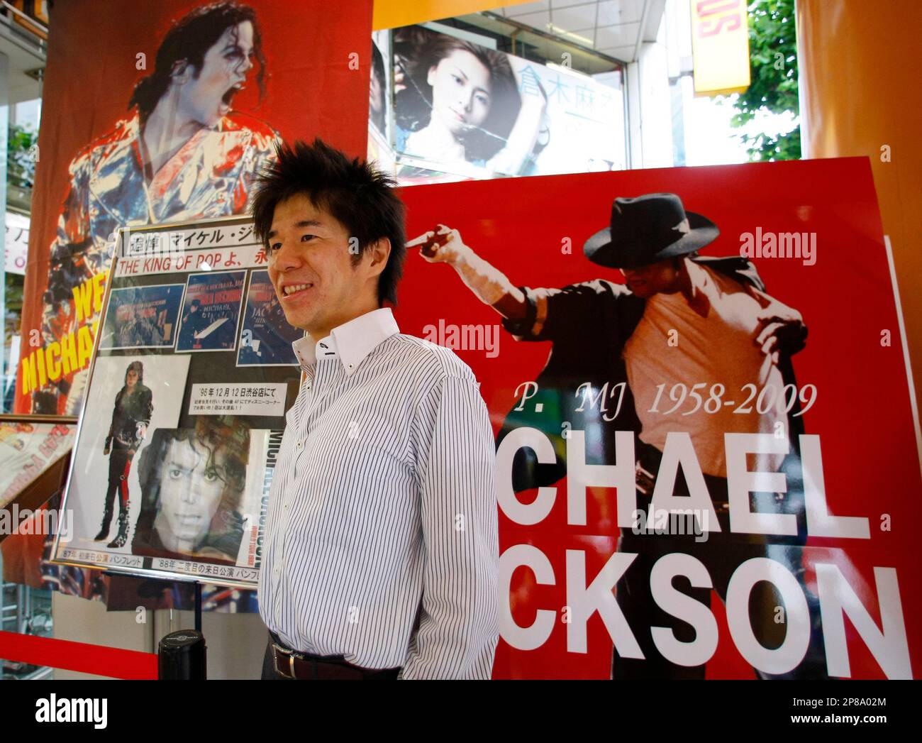 A Japanese fan stands in front of a Michael Jackson poster for a commemorative photo at a Tower Records store in downtown Tokyo Tuesday, July 7, 2009. Japanese fans gathered at the store for a memorial for the pop legend ahead of the extravaganza set to open later in Los Angeles. (AP Photo/Shizuo Kambayashi) Stockfoto