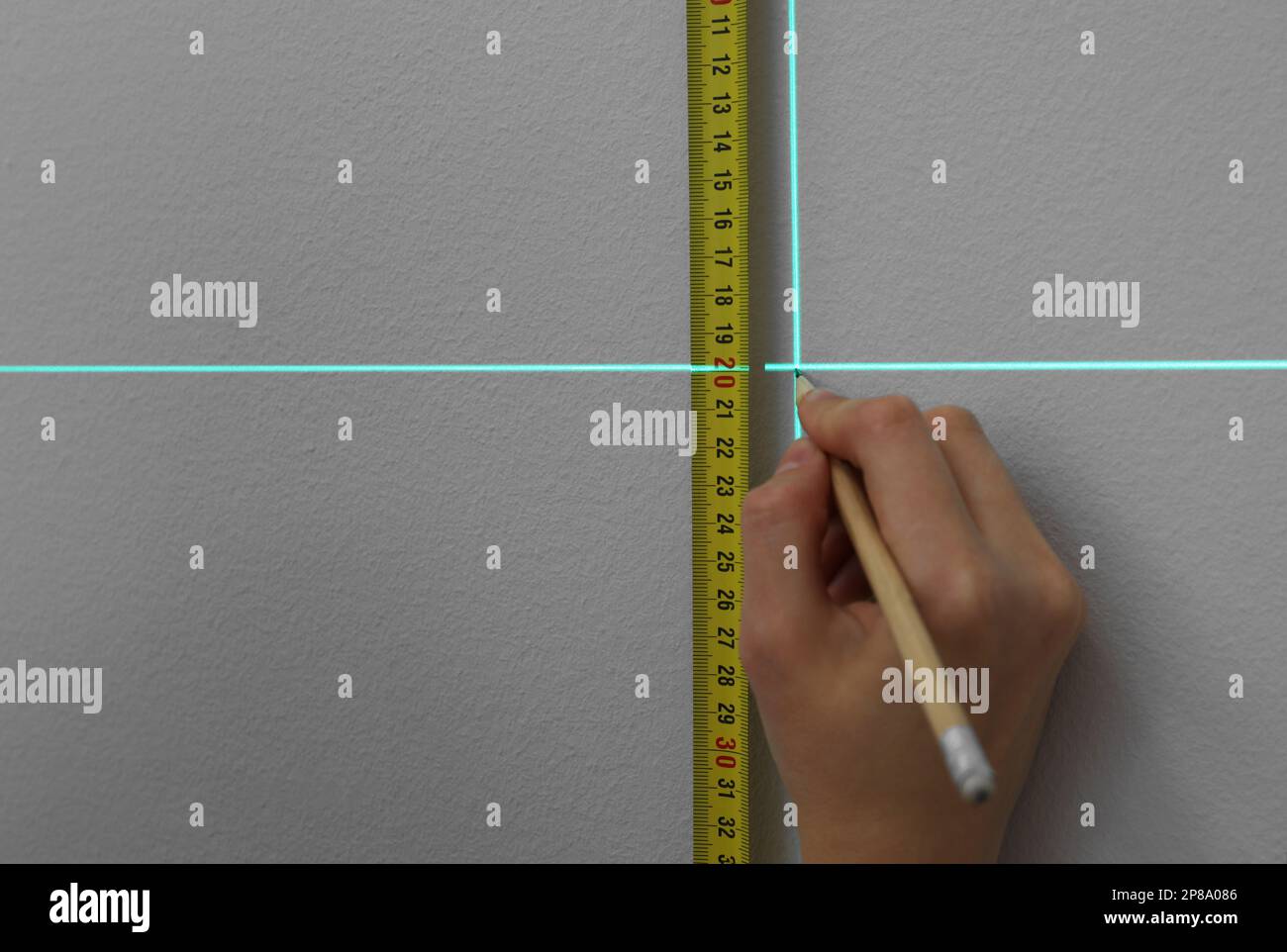Frau, die Kreuzlinienlaser-Nivelliergerät, Klebeband und Bleistift für genaue Messungen an grauen Wänden und Nahaufnahmen verwendet Stockfoto