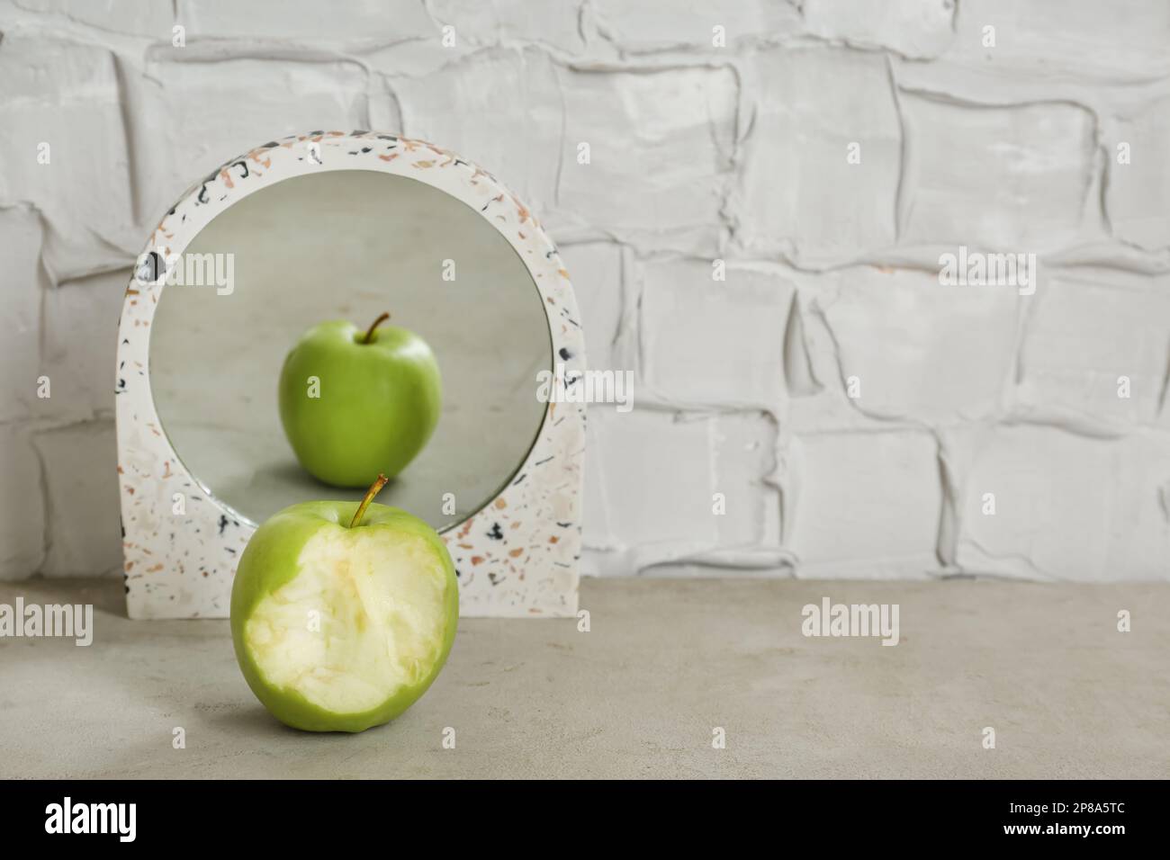 Gebratener grüner Apfel neben dem Spiegel mit Reflexion von ganzen Früchten auf dem Tisch, Platz für Text Stockfoto