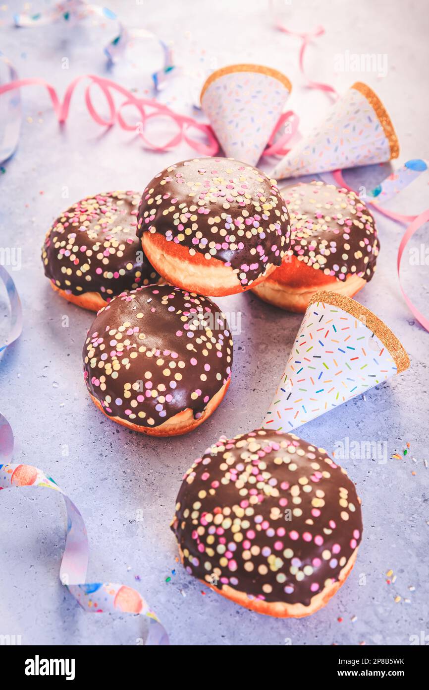 Schokoladen-Berliner-Gebäck für Karneval und Party. Deutsche Krapfen oder Donuts mit Bändern und Konfetti. Farbenfrohes Karneval- oder Geburtstagsbild Stockfoto