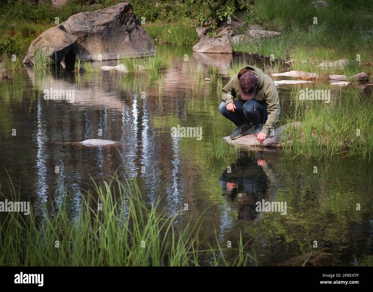 Eine Frau, die auf einem Felsen hockt und ins Wasser blickt: Lake Lemolo, Oregon, USA Stockfoto