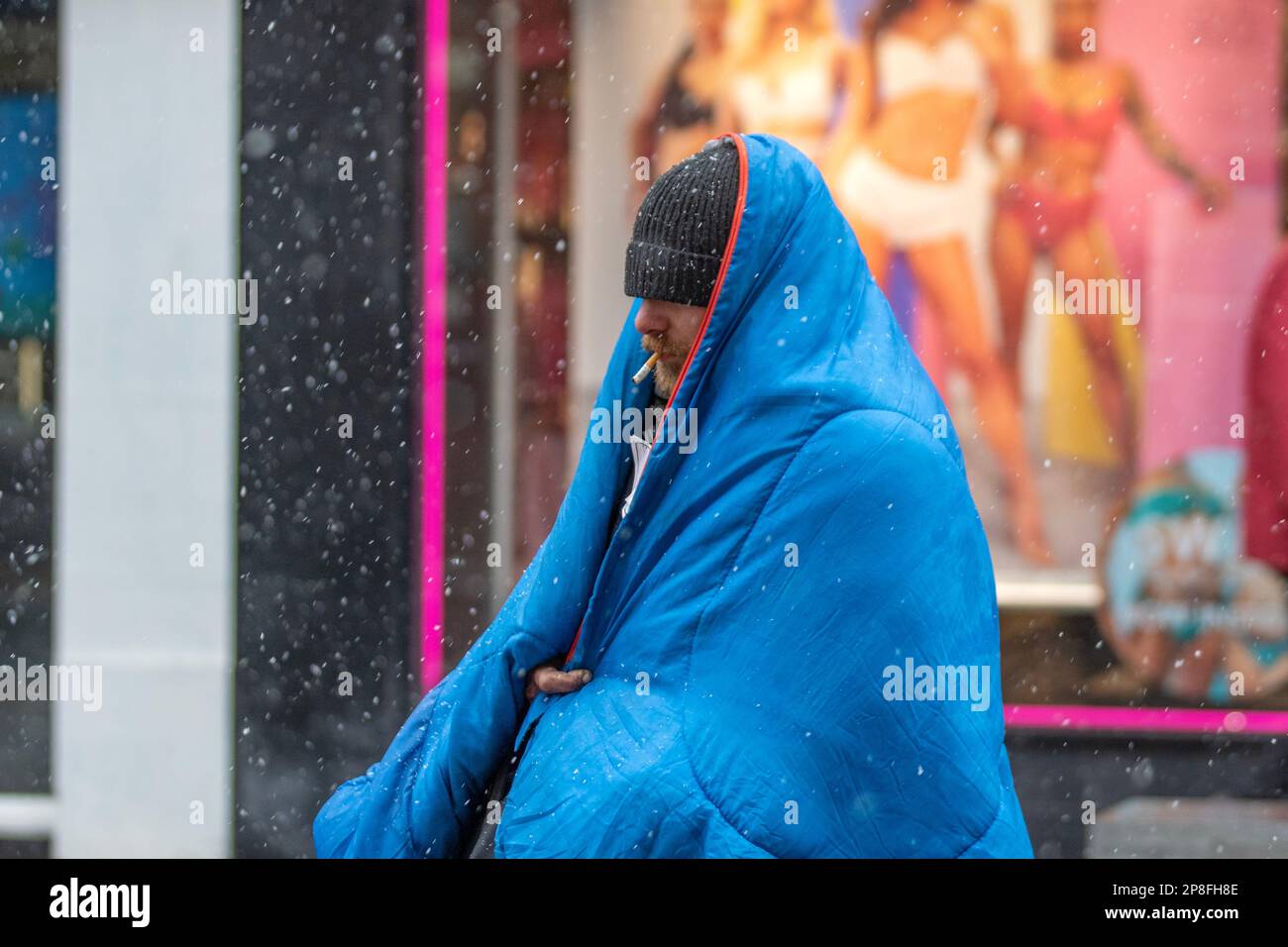 Obdachlose, eingewickelt in Federdecke in Preston, Lancashire. Wetter in Großbritannien, 9. März 2023. Obdachlose an einem Wintertag im Stadtzentrum, an einem Tag mit Schnee und Graupelschauern. Die Vorhersage ist für wolkigen Himmel und weitere Schneeperioden, die aus dem Westen herankommen, die manchmal schwer werden. Kredit; MediaWorldImages/AlamyLiveNews Stockfoto