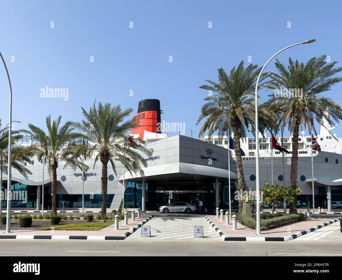 Das Auto parkte am Hoteleingang mit dem Schiff Queen Elizabeth 2 im Hintergrund. Stockfoto Das Auto parkte am Hoteleingang mit dem Schiff Queen Elizabeth 2 im Hintergrund. Stockfoto