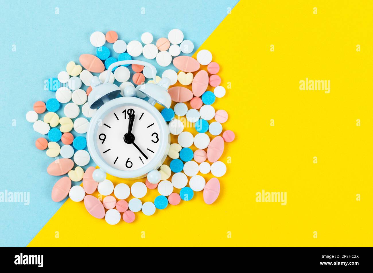 Pillen und Wecker auf blauem und gelbem Hintergrund Stockfoto
