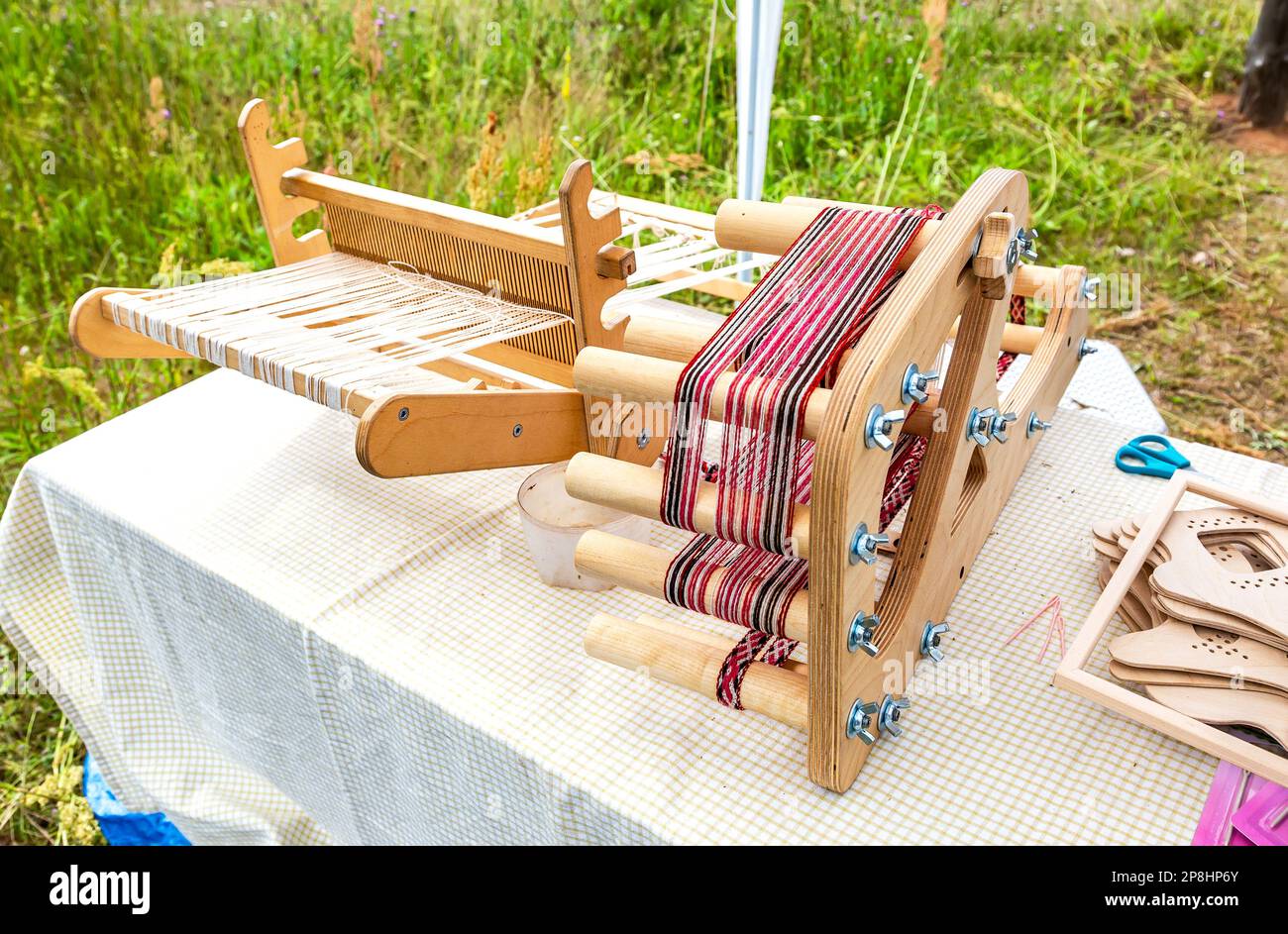 Handgefertigter HolzWebstuhl mit rot-weißen Wollen im Freien im Sommer Stockfoto