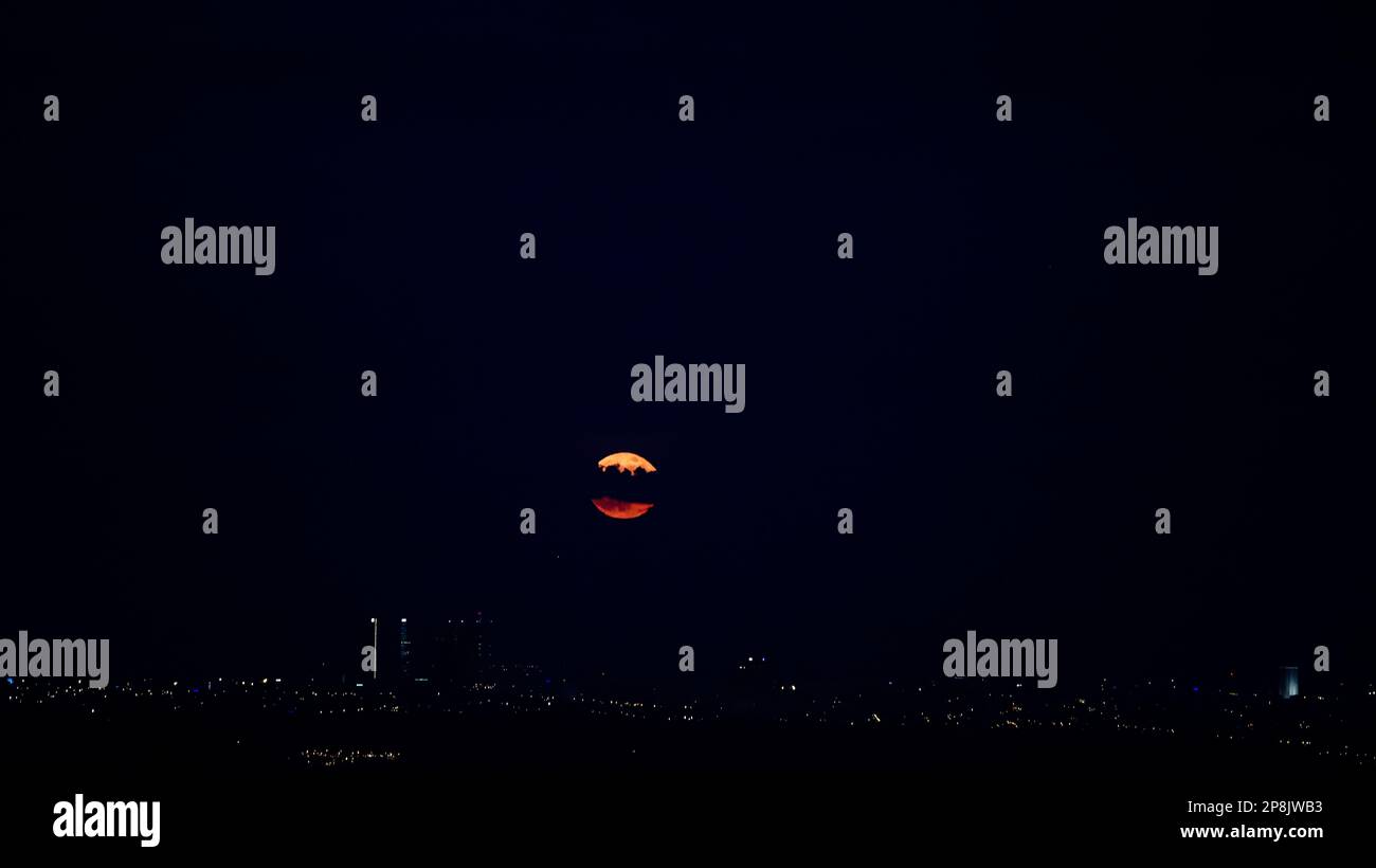 Roter Mond der Sonnenfinsternis zwischen den Wolken, die zwischen Gebäude einer Stadt fallen Stockfoto