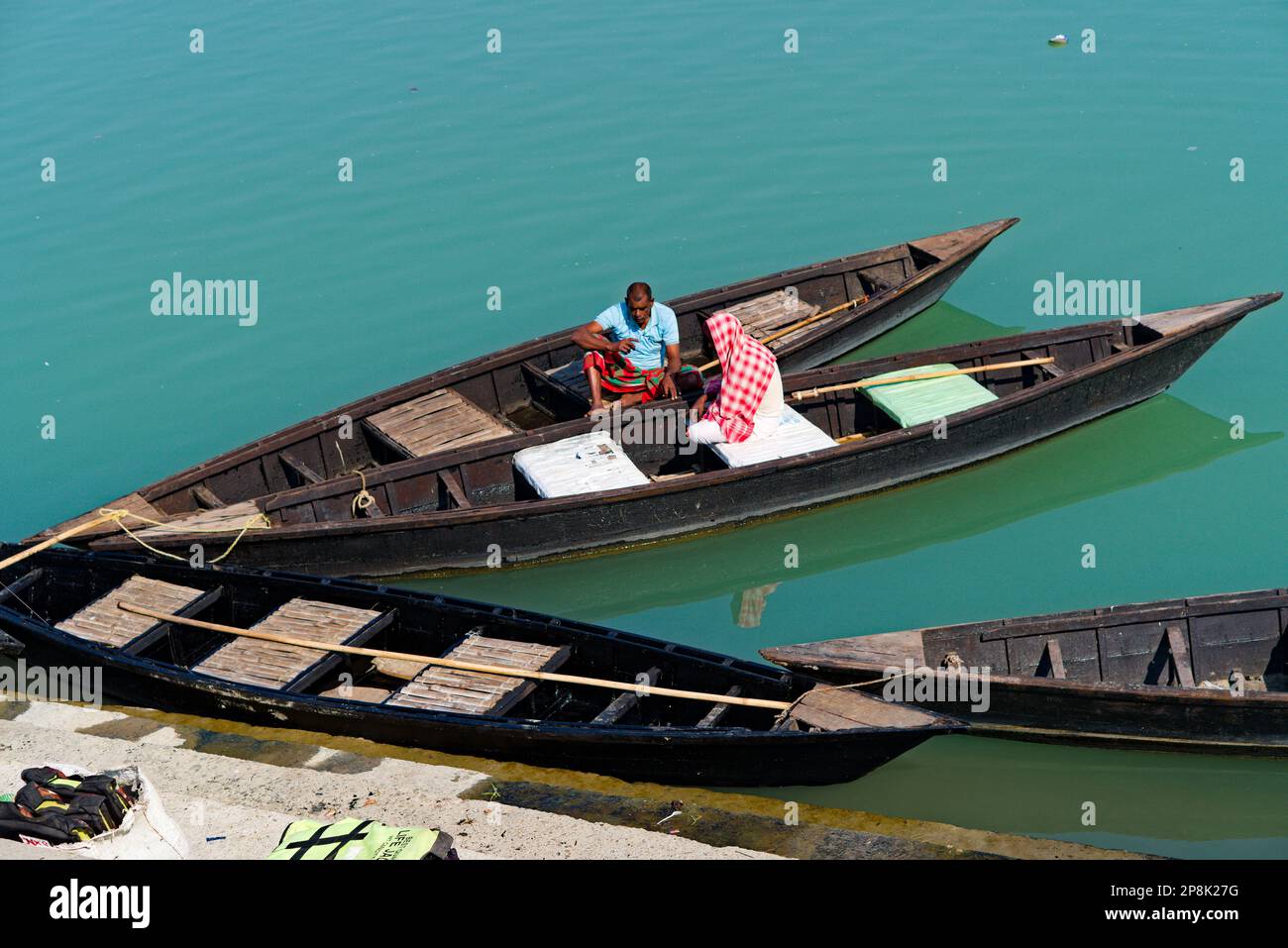 Bootsfahrer sitzen auf einem Holzboot am Flussufer Stockfoto