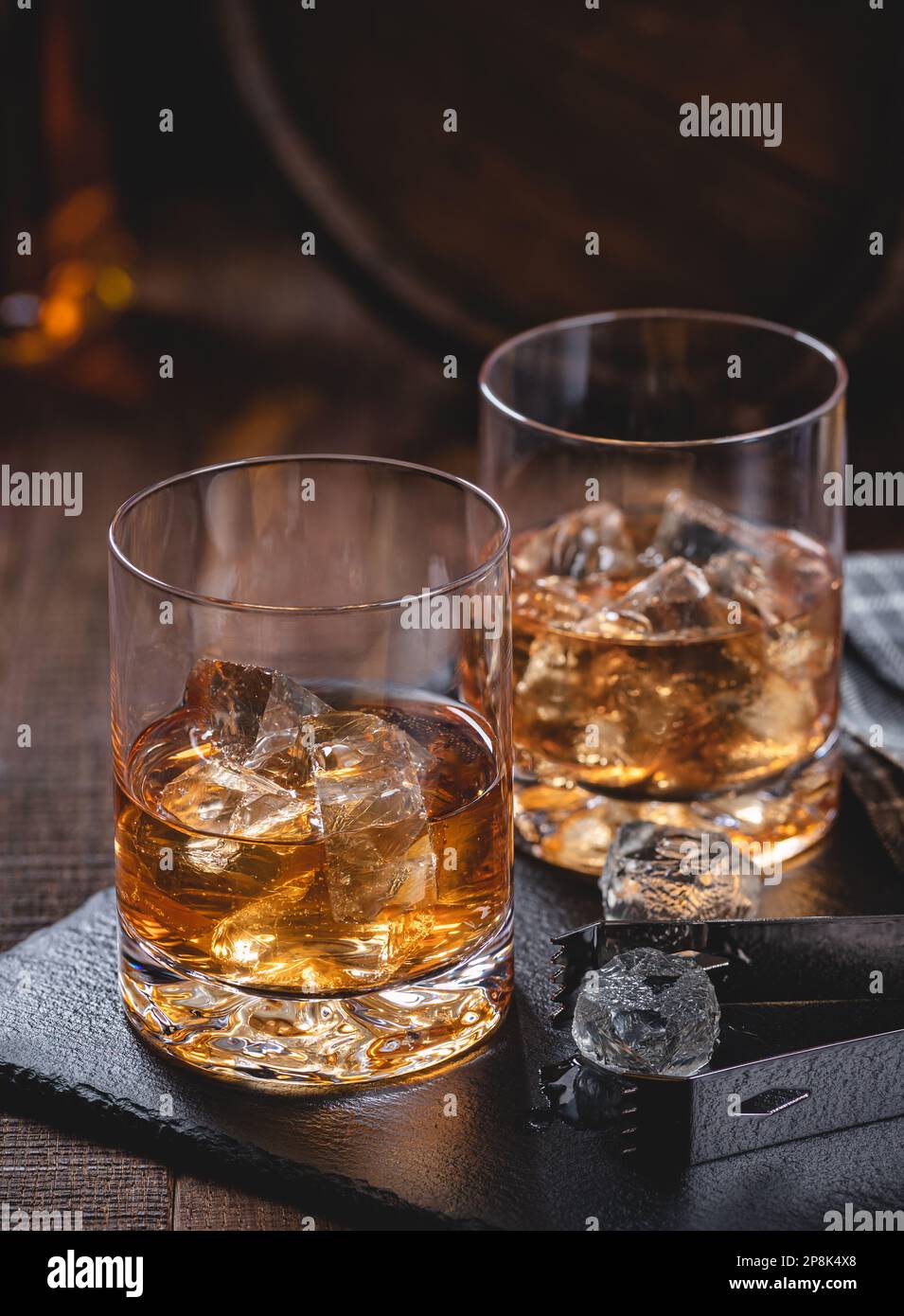 Zwei Gläser Whiskey mit Eis auf einem schwarzen Schieferbrett mit Holzhintergrund Stockfoto