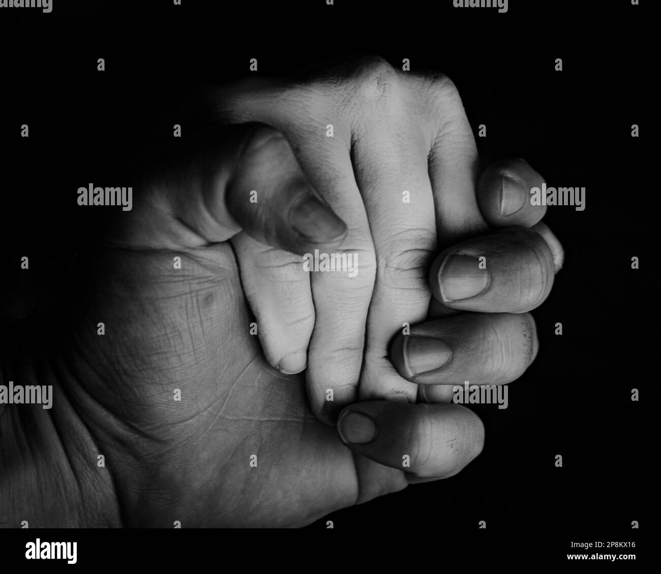 Eine Großaufnahme in Graustufen, bei der Hände vor schwarzem Hintergrund gehalten werden. Stockfoto