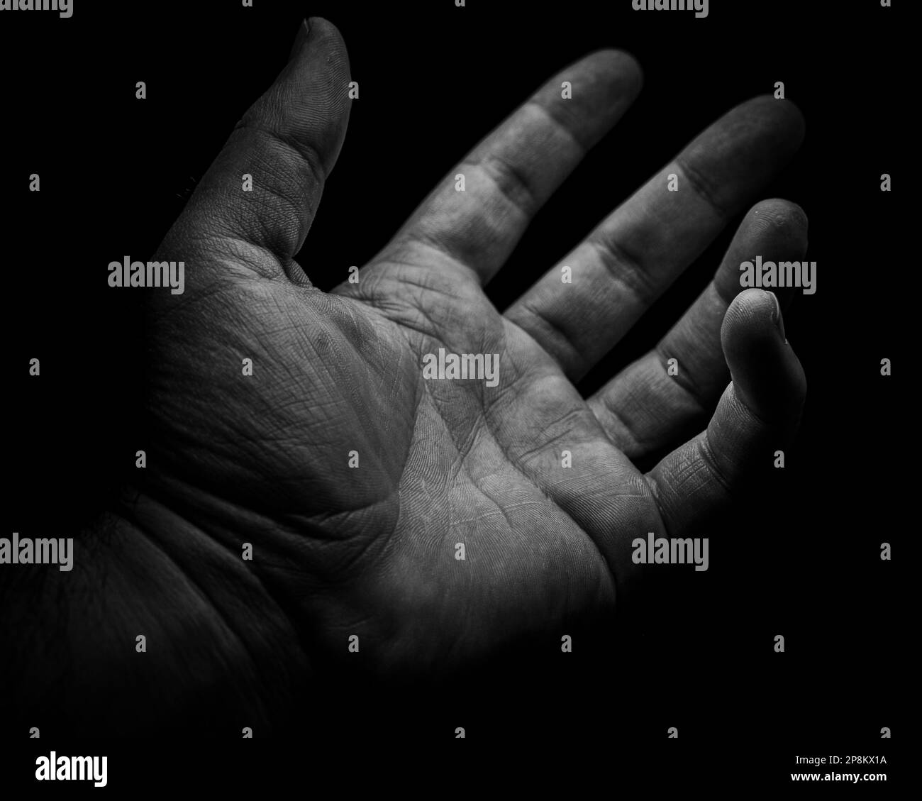 Eine Graustufenaufnahme einer menschlichen Hand, die auf ein unbekanntes Wesen vor schwarzem Hintergrund greift. Stockfoto