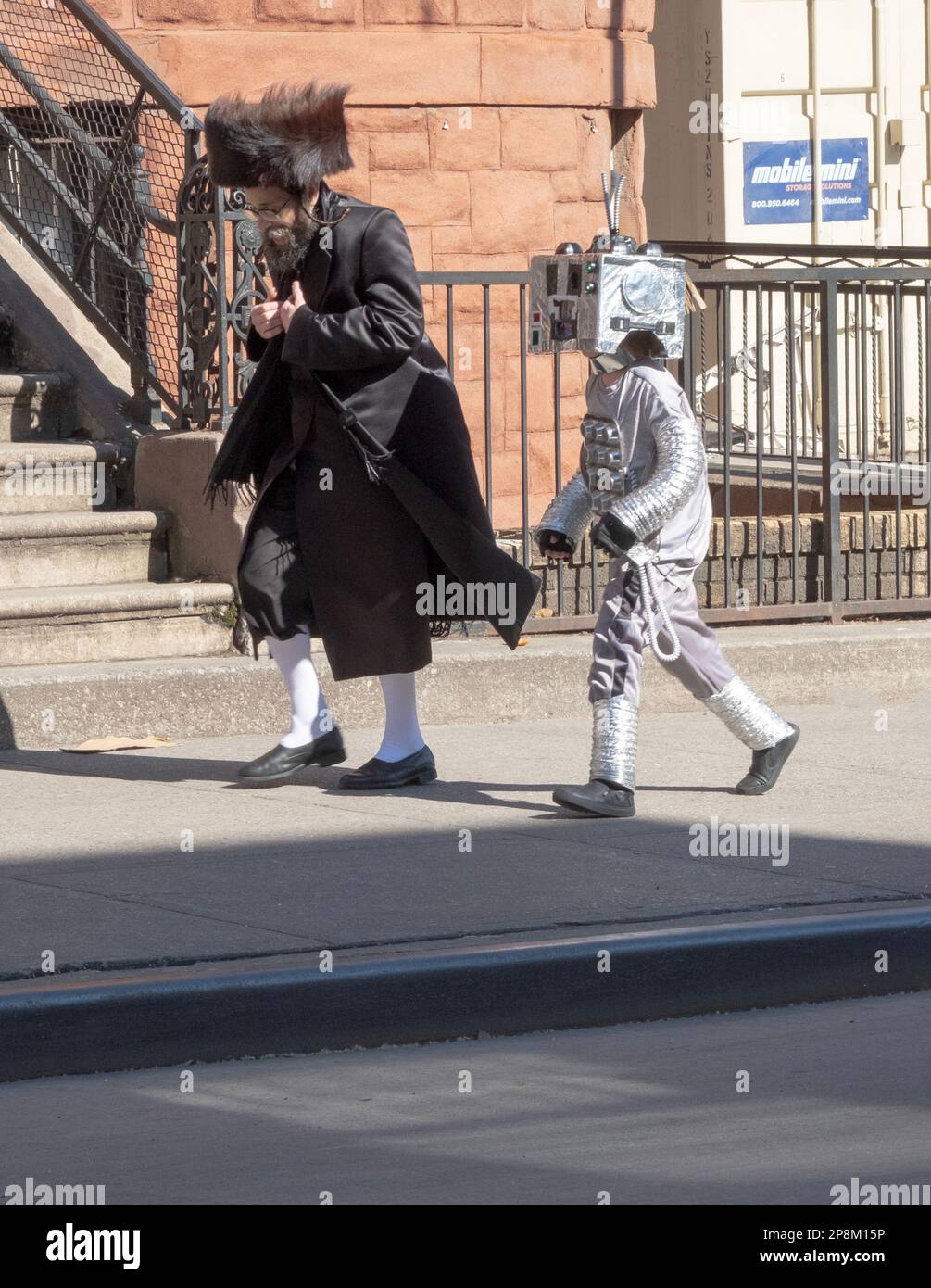 Ein Vater und sein Sohn gehen auf der Bedford Avenue in Brooklyn auf der Purim. Der Junge ist als Raumfahrer verkleidet und Dad trägt einen Shtreimel. In Brooklyn, New York. Stockfoto