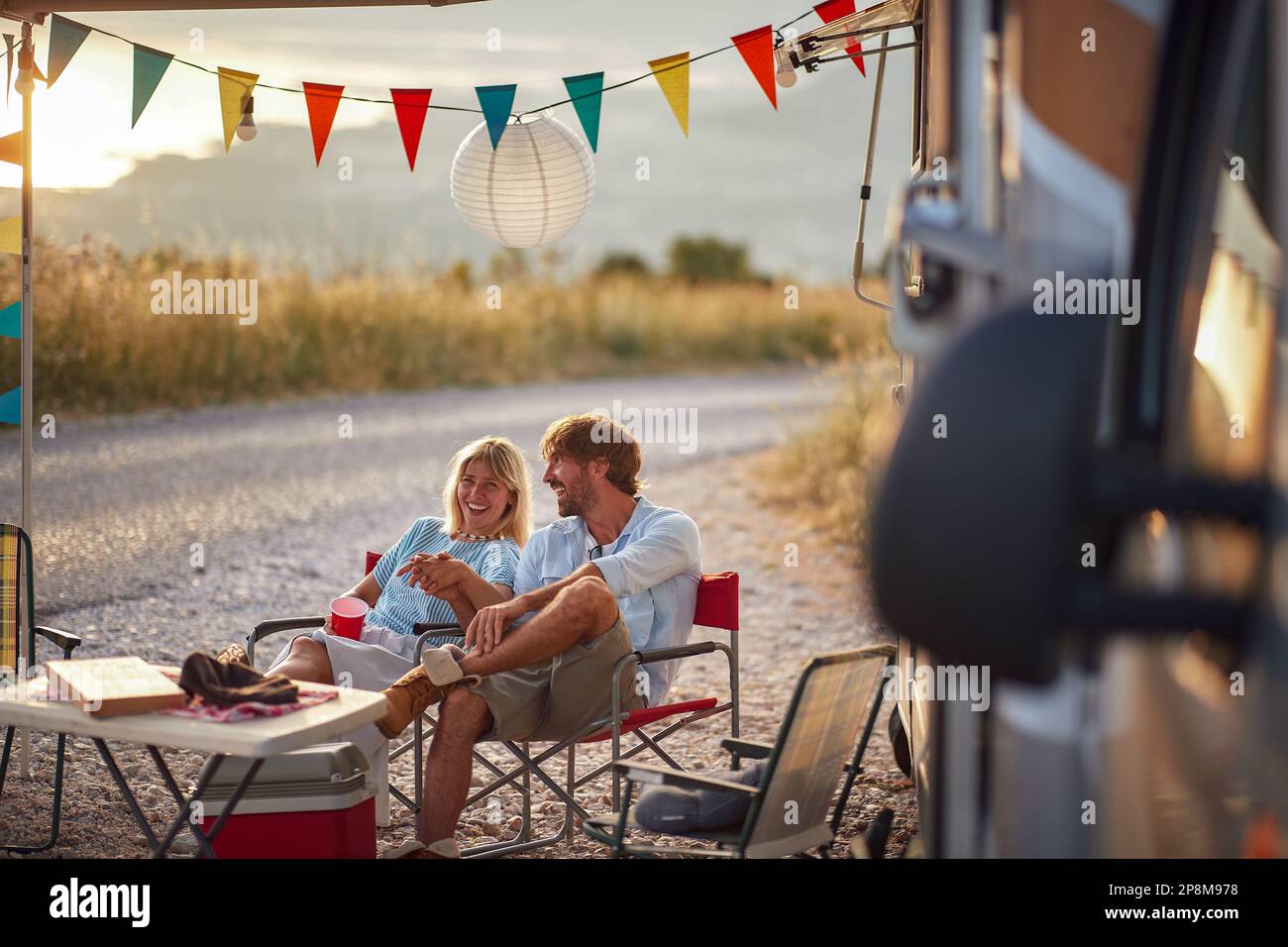 Hübsches, junges erwachsenes Paar, das draußen vor einem Wohnmobil sitzt, Händchen hält, lacht. antistress-Konzept Stockfoto