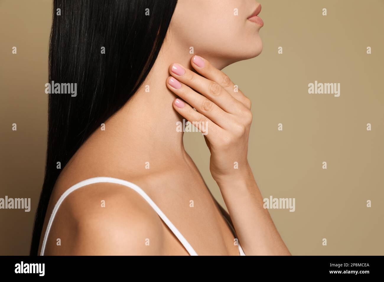 Junge Frau, die Schilddrüsen-Selbstuntersuchung auf beigefarbenem Hintergrund macht, Nahaufnahme Stockfoto
