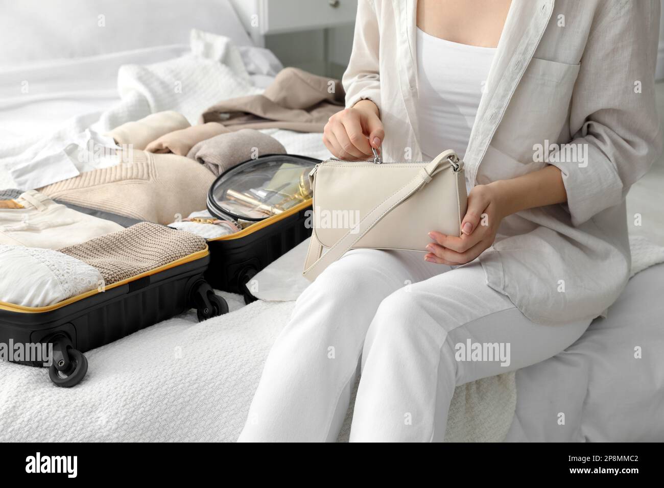 Eine Frau mit Handtasche, die neben einem offenen Koffer auf dem Bett im Zimmer sitzt Stockfoto