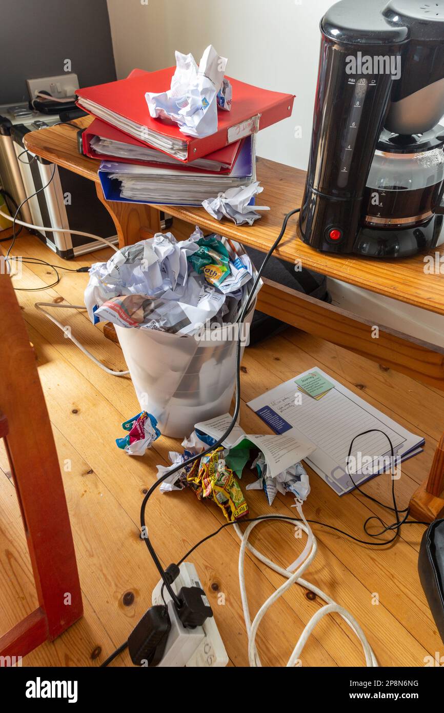 Ein chaotisches Heimbüro mit einem überfüllten Abfalleimer und einer Kaffeemaschine. Stockfoto