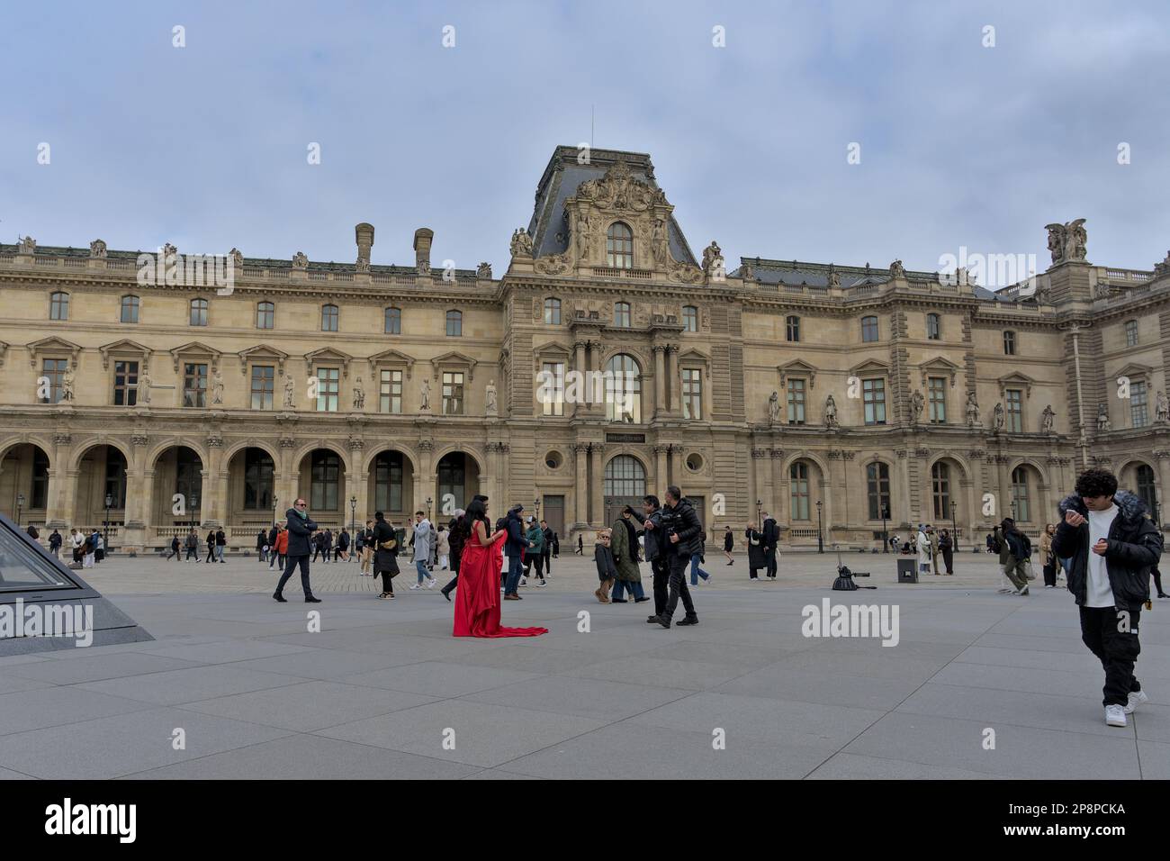 Ein Paar in Rot, das vor dem Louvre fotografiert wird, mit Touristen in der Nähe Stockfoto