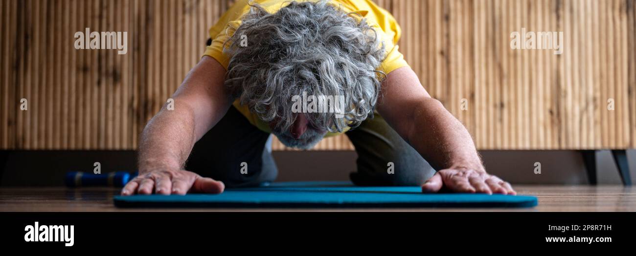 Breites Sichtbild eines aktiven Seniorenmannes, der sich im Ruhestand um seine Gesundheit kümmert. Beim Yoga oder Pila auf einer Matte trainieren, sich in der Kinderhaltung ausstrecken Stockfoto