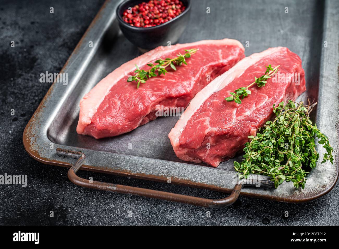 Filetsteak der Spitzenklasse, rohes Rindfleisch-Steak mit Thymian und Pfeffer auf einem Stahltablett. Schwarzer Hintergrund. Draufsicht. Stockfoto