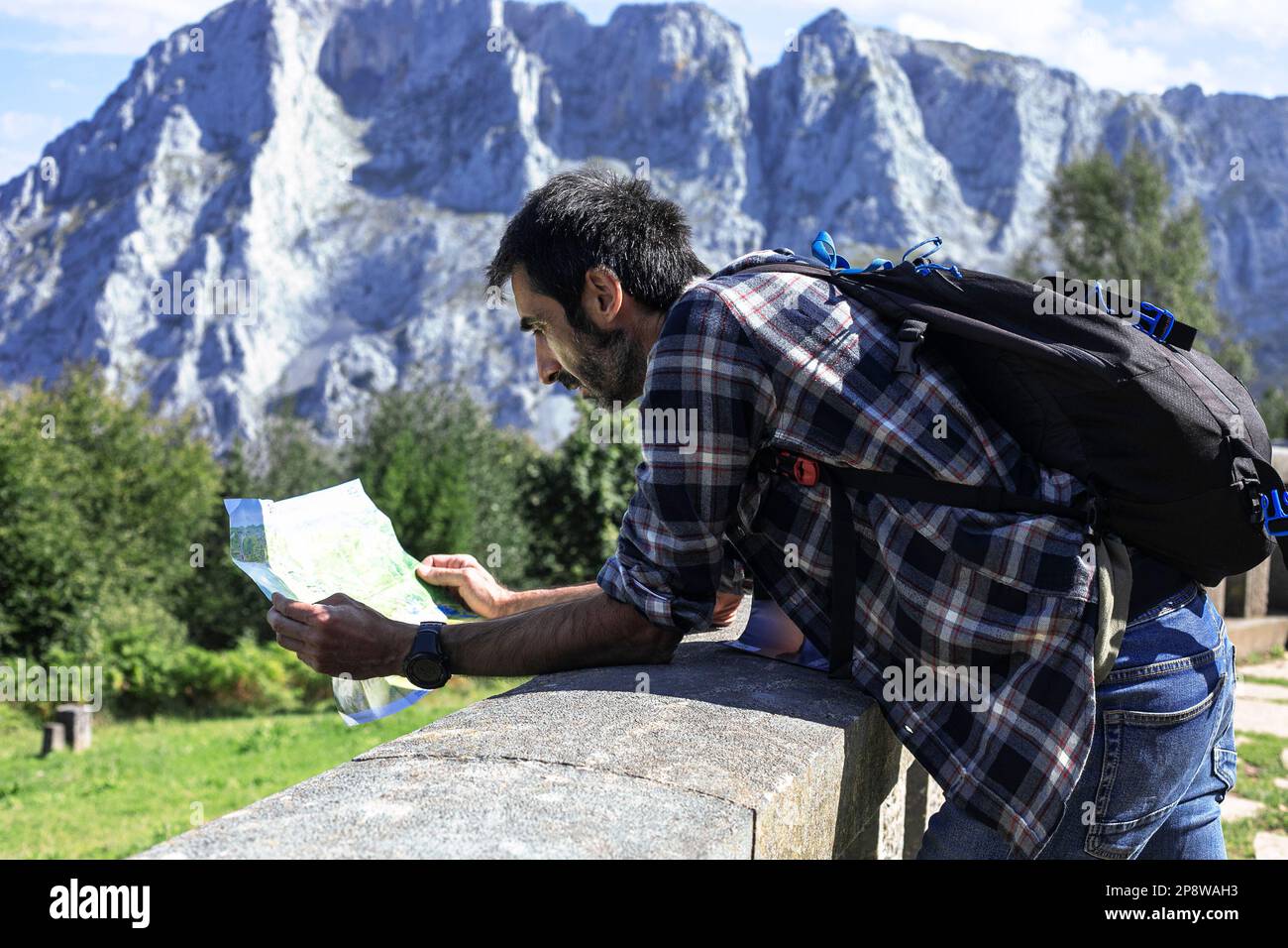 An einem sonnigen Tag schaut ein Wanderer mit Rucksack auf eine Karte in einem Naturpark. Urkiola Naturpark, Baskenland. Stockfoto