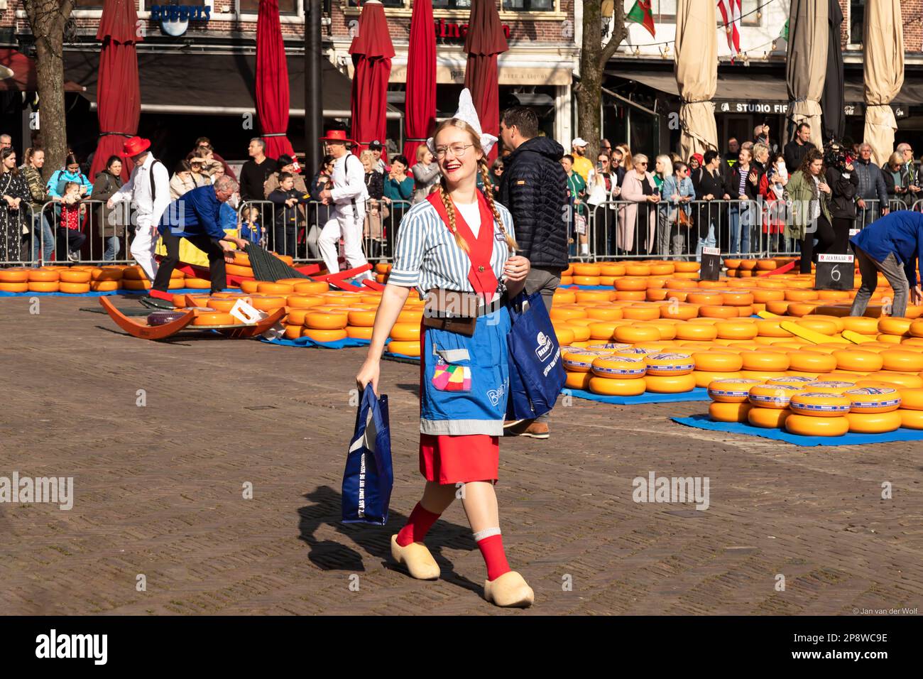 Das Käsemädchen in traditionellem Kostüm und Holzschuhen geht mit ihren Waren lächelnd durch den Käsemarkt in der Stadt Alkmaar. Stockfoto