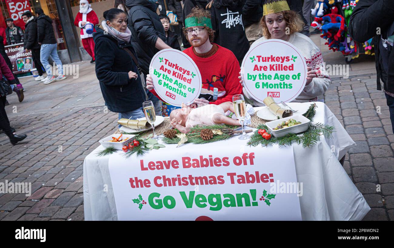 Ein Mann und eine Frau sitzen an einem Weihnachtstisch in der Market Street, der mit Babys gekleidet ist, anstatt mit der türkei, um die Go Vegan Kampagne zu fördern Stockfoto