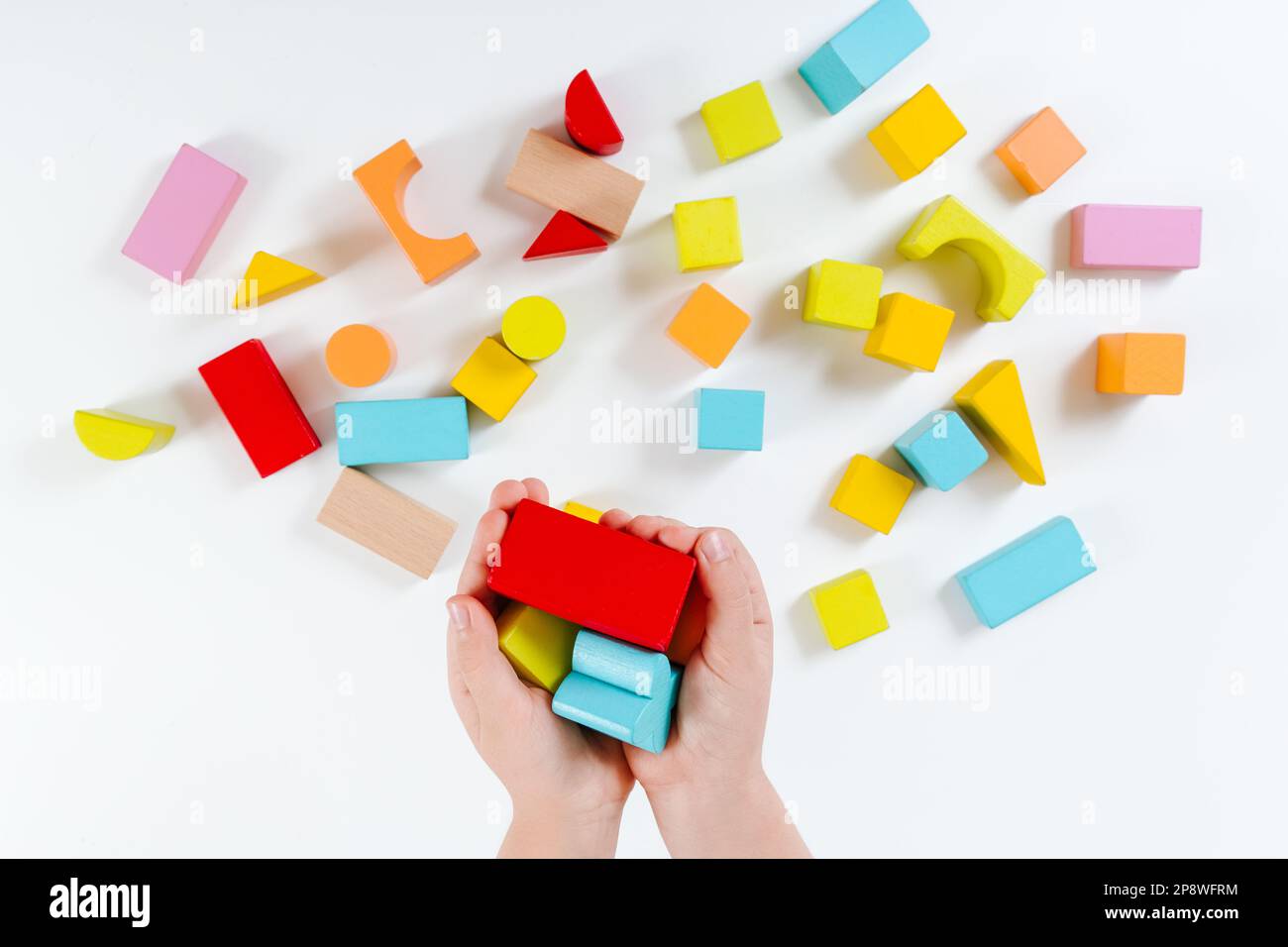Kinderhände spielen mit bunten Holzsteinen. Spielset aus Holz. Entwicklungs- und Lernkonzept. Weißer Hintergrund. Flach verlegt. Natürliche Materialien. Stockfoto