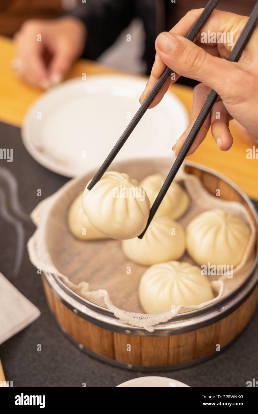 Hand mit Stäbchen, die köstliche Knödel aus der traditionellen Schüssel nehmen, gesunde Speisen bereit zum Essen im Restaurant, asiatische Tradition Stockfoto