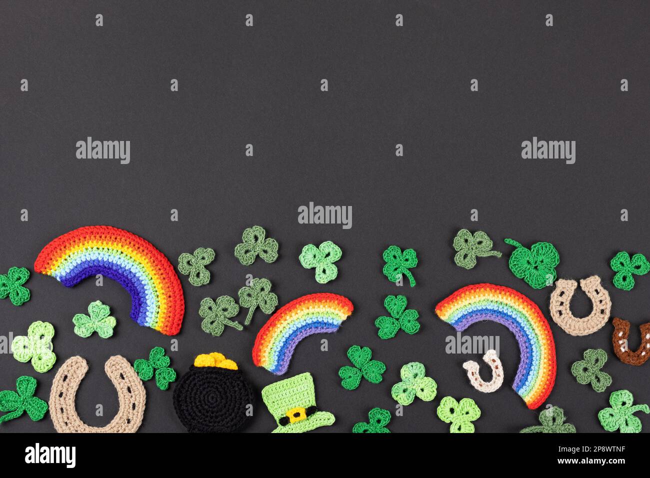 St. Patrick's Day Konzept. Gestrickte Komposition aus grünem Hut, goldenem Topf, Hufeisen, Regenbogen und grünen Shamrocks auf schwarzem Hintergrund Stockfoto