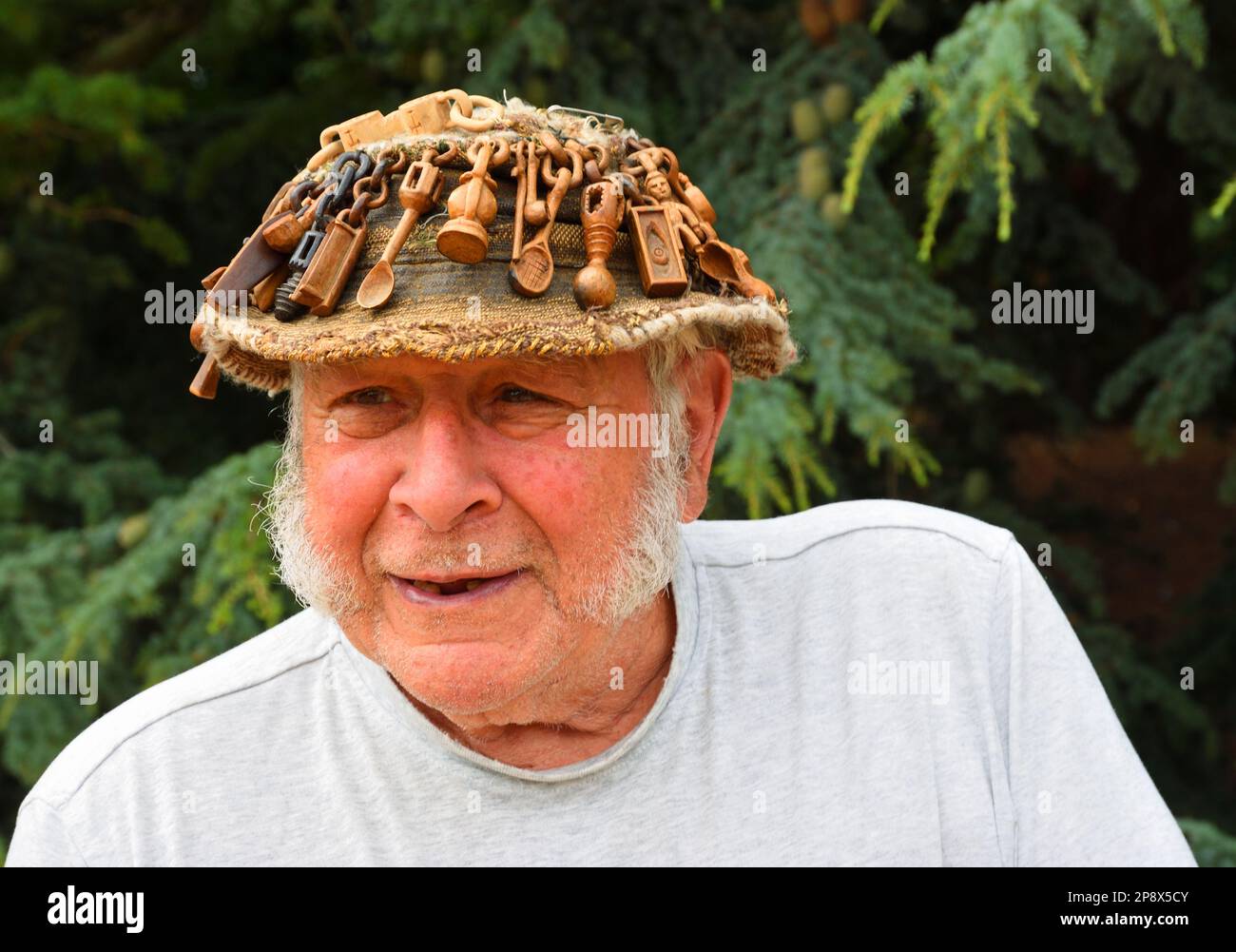 OXBOROUGH, NORFOLK, ENGLAND - 12. JULI 2022: Älterer Mann mit Hut, der mit geschnitzten Liebeslöffeln aus Holz bedeckt ist. Stockfoto