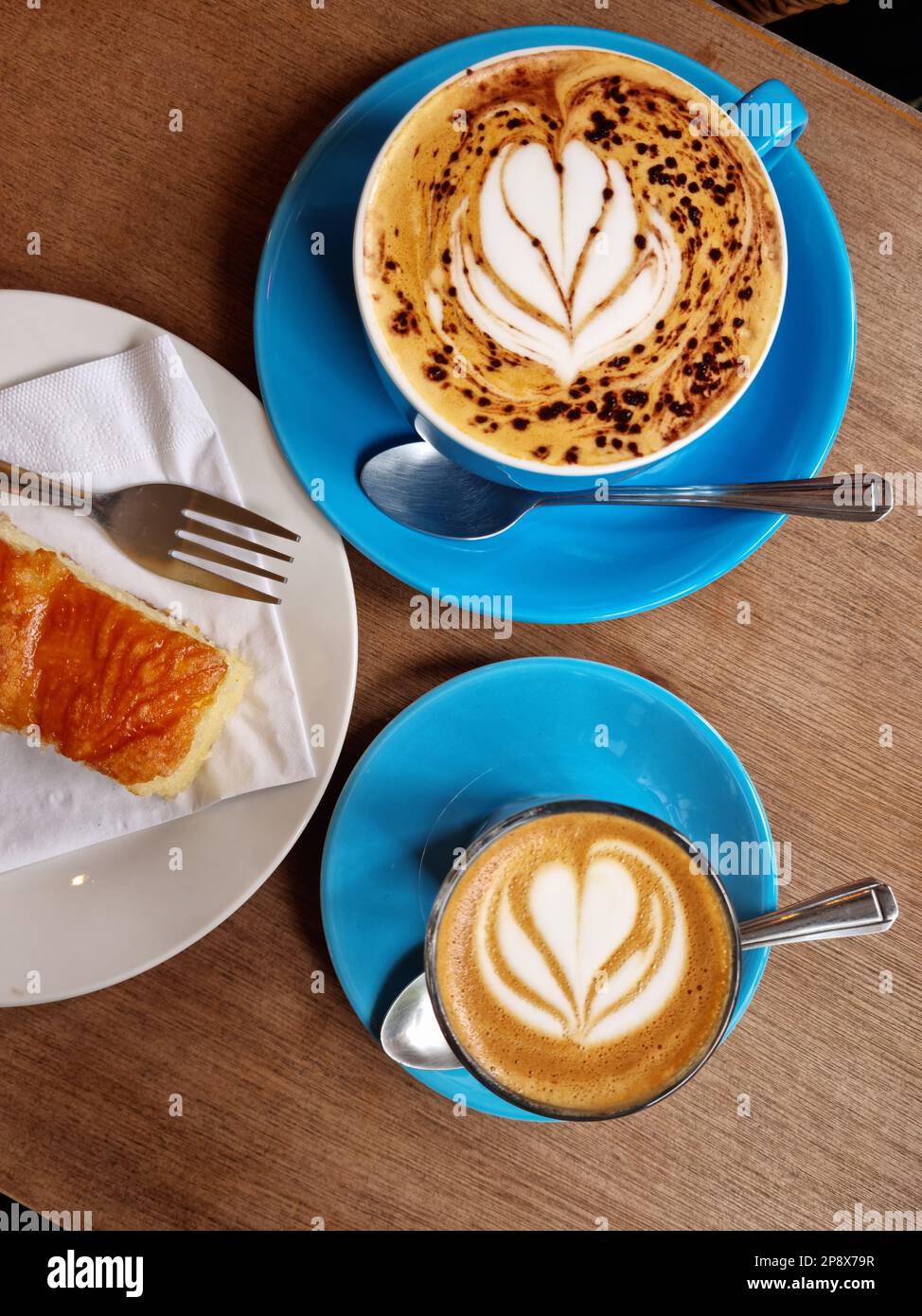 Blick von oben auf dekorierte Tassen Kaffee (Kaffeekunst) und ein Stück Zitronenkuchen Stockfoto