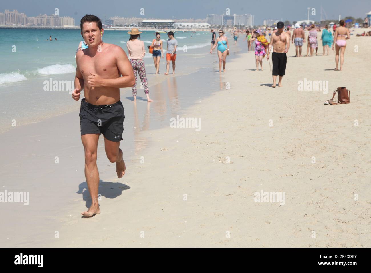 Junge Briten in kurzen Hosen genießen Barfußlaufen und Sonnenbad am Sandstrand von Dubai im Februar, und andere kaukasische Leute profitieren vom 27C. Winter Stockfoto