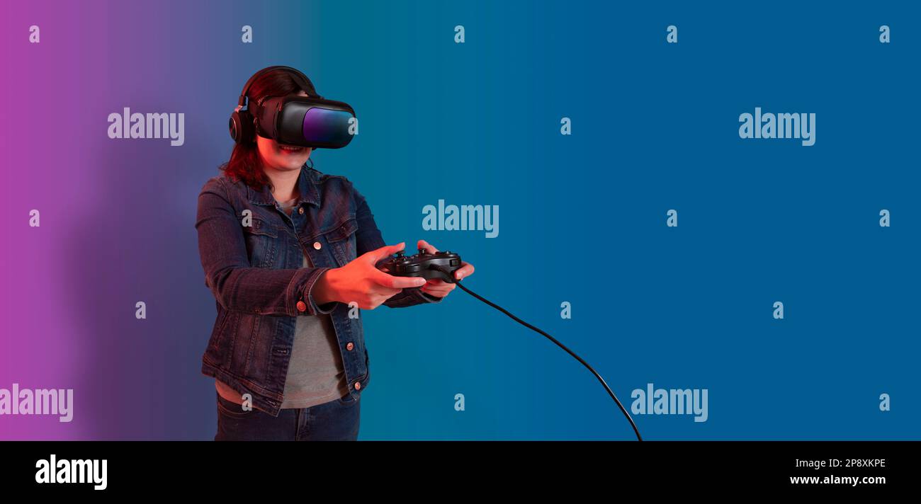 Wunderschöne junge hispanische Frau, die mit einer Virtual-Reality-Brille steht und mit einer Videospielkonsole in ihren Händen gegen den lilafarbenen blauen Backgro spielt Stockfoto