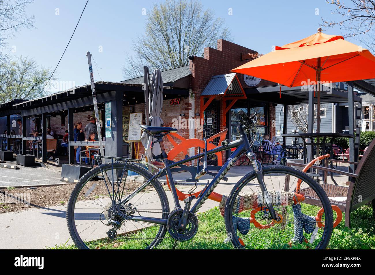 CHARLOTTE, NC-5. MÄRZ 2023: Bezirk Noda. Stinkendes Cat Coffeehouse. Fahrrad im Vordergrund geparkt, Kunden unter einem Sonnenschirm. Stockfoto