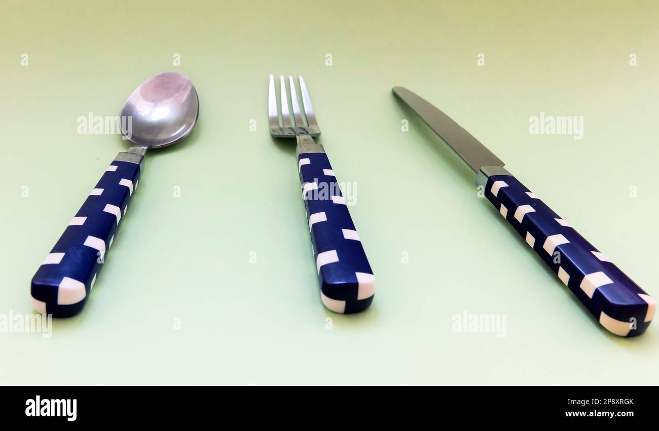 Blauer und weißer Kontrolllöffel, Gabel, Messer auf grünem Hintergrund Stockfoto