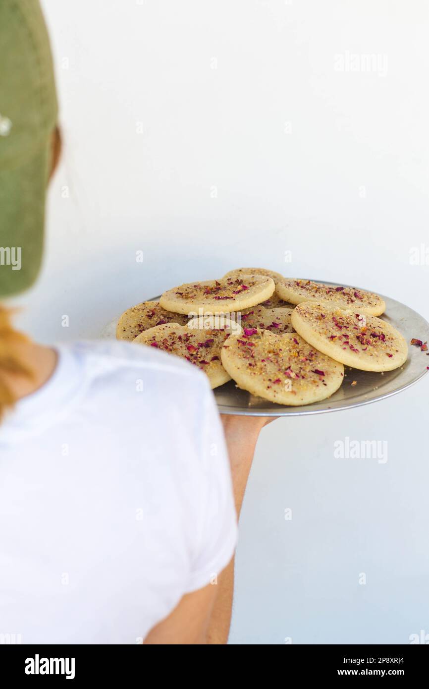 Eine Bäckerin hält ein Tablett mit Keksen über ihrer Schulter auf einem einfachen weißen Hintergrund. Stockfoto