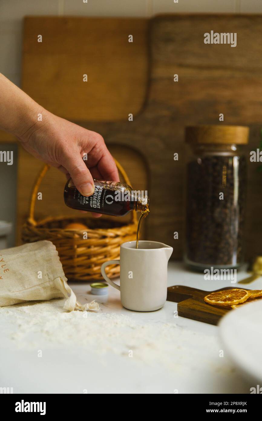 Bei der Zubereitung von Pfannkuchen gießt eine Hand Sirup in einen kleinen Keramikkrug Stockfoto