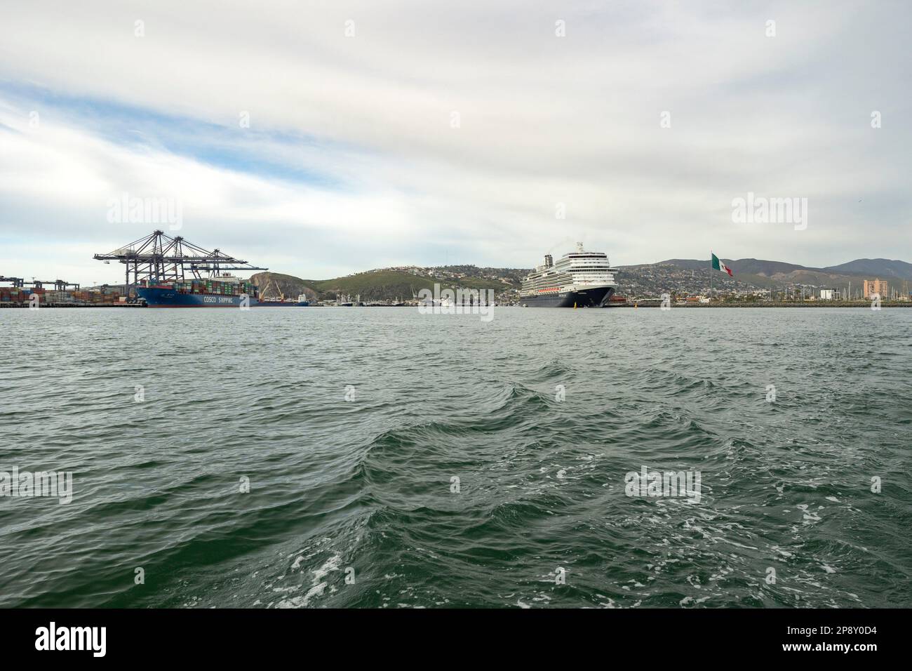 Ensenada, Baja California, Mexiko - Blick vom Ozean des Hafens mit angedocktem Frachtschiff und Kreuzfahrtschiff Stockfoto