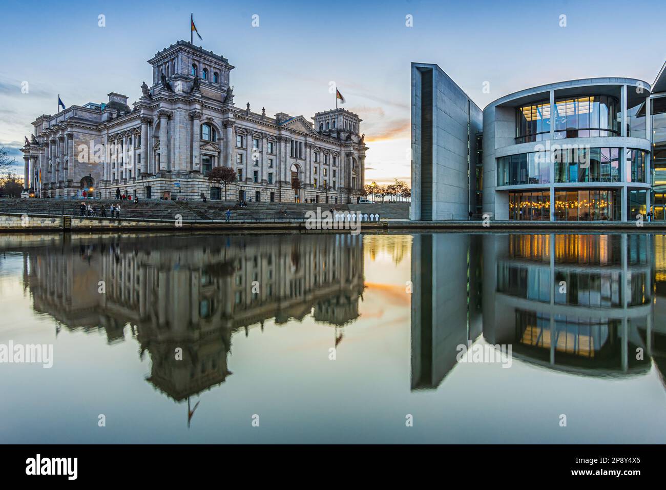 Sonnenuntergang im Zentrum von Berlin. Regierungsgebäude Paul Löbe Haus und Reichstag mit Reflexion auf der Oberfläche des Flusses. Beleuchtete Fassade Stockfoto