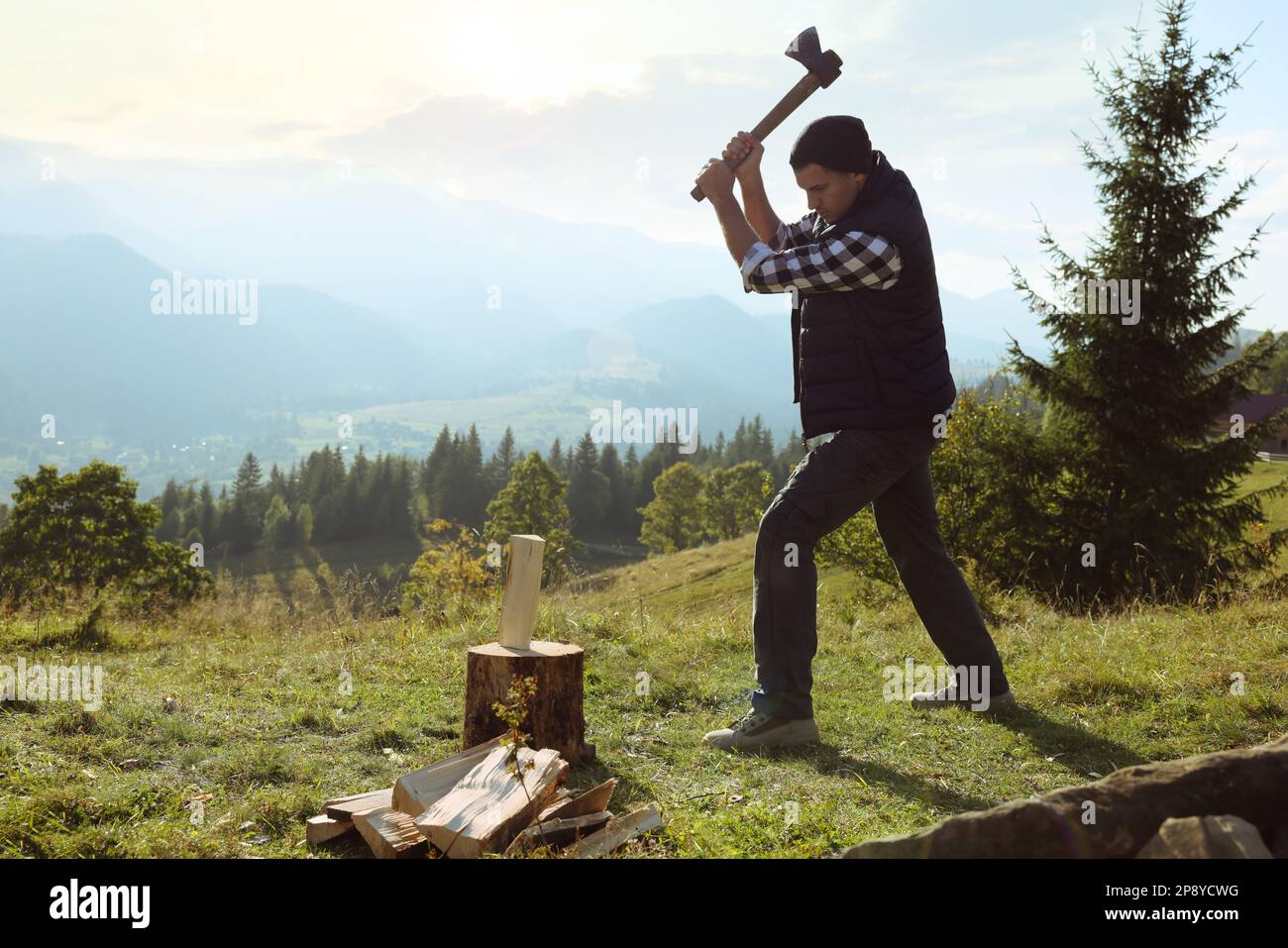 Ein gutaussehender Mann mit Axt, der auf dem Hügel Brennholz schneidet Stockfoto Ein gutaussehender Mann mit Axt, der auf dem Hügel Brennholz schneidet Stockfoto
