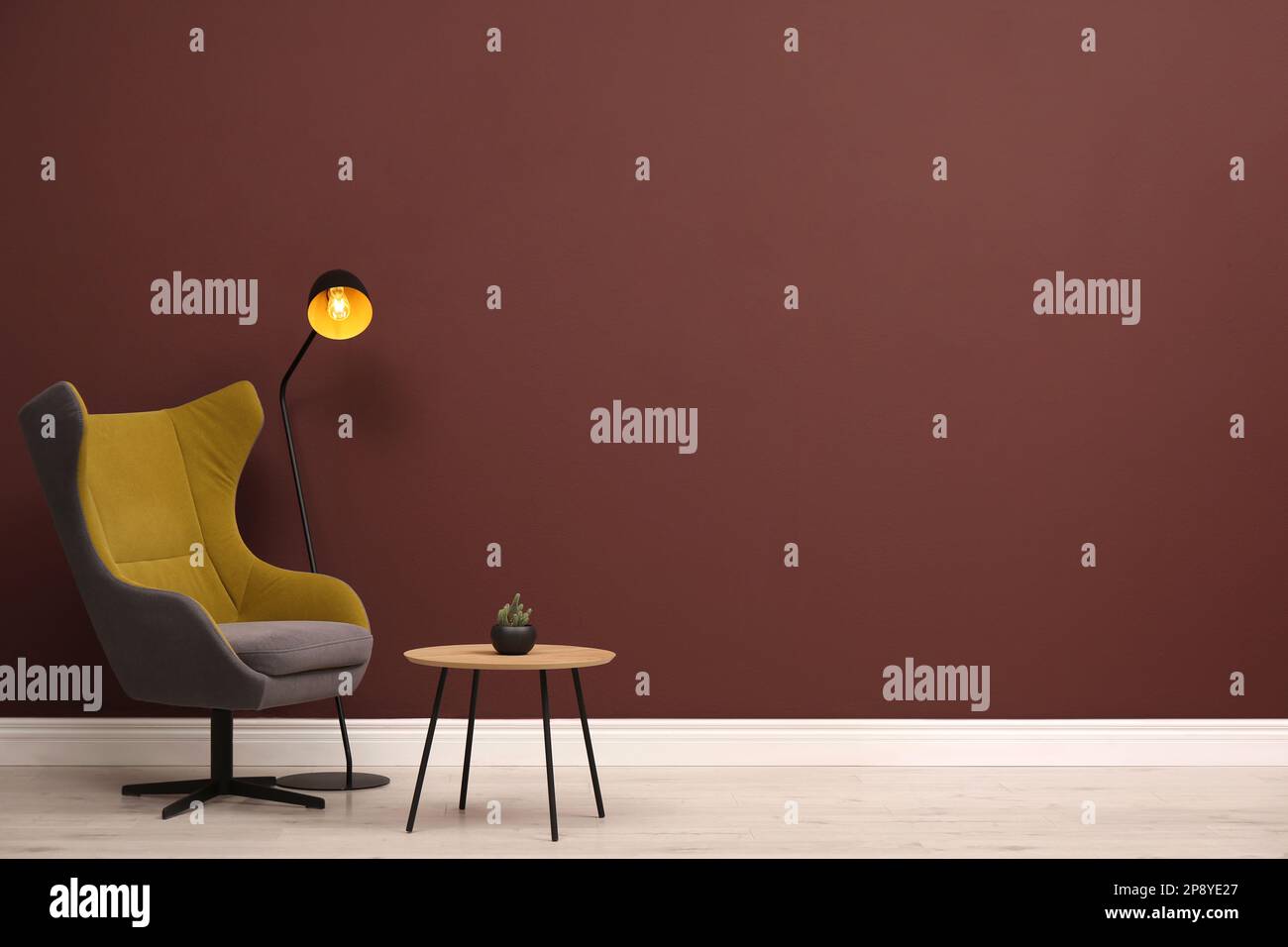 Eleganter Sessel, Tisch und Lampe nahe der braunen Wand, Platz für Text Stockfoto