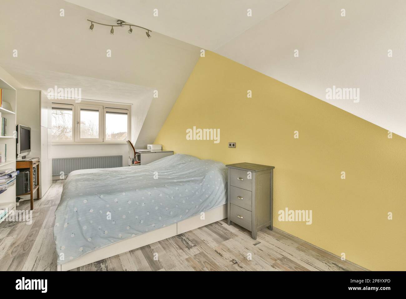 Ein Schlafzimmer mit gelben Wänden und Holzfußboden an der Wand, es gibt einen Fernseher in der Ecke neben dem Bett Stockfoto
