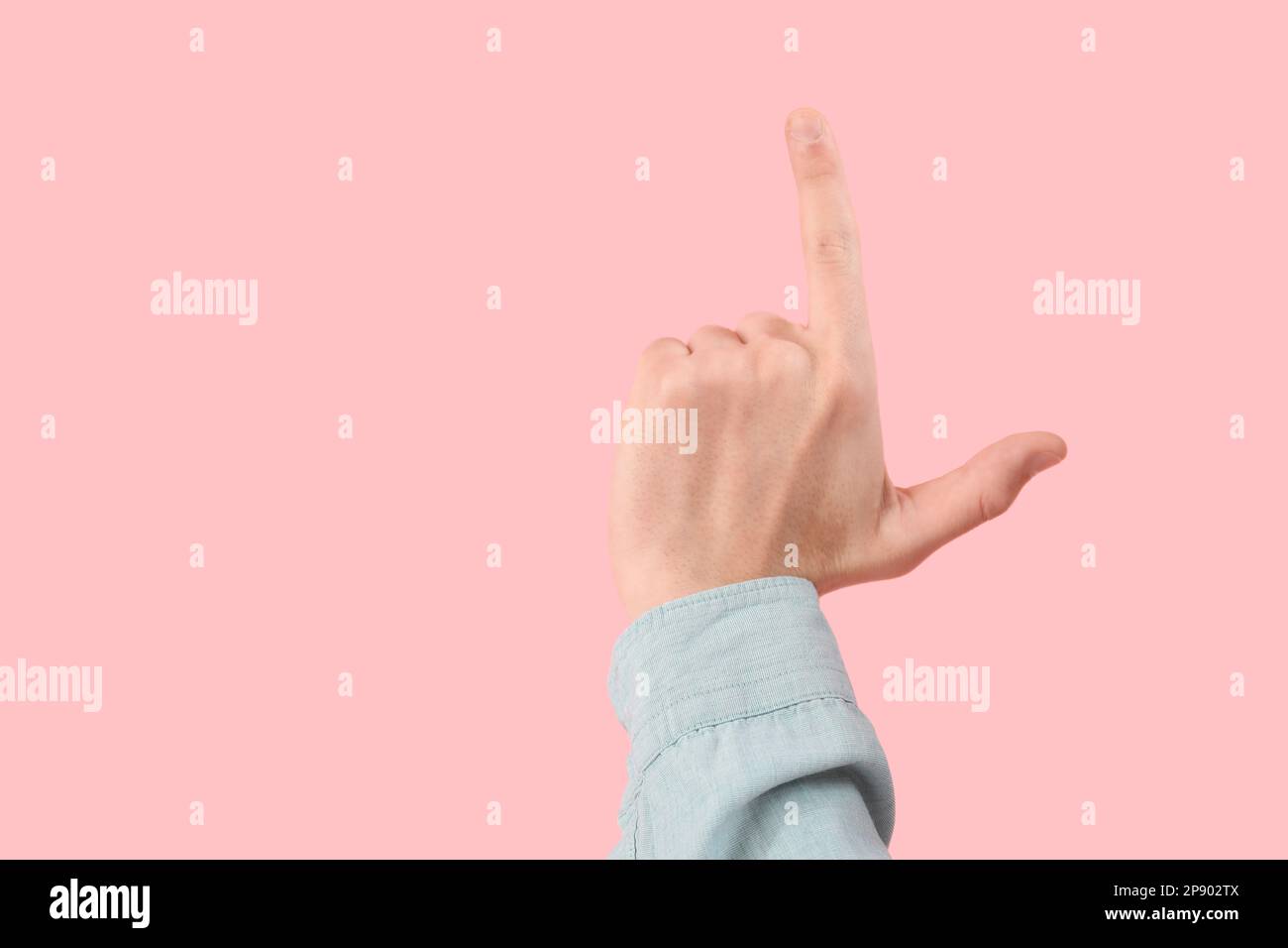 Die Hand eines Mannes zeigt eine Verlierer-Geste auf pinkfarbenem Hintergrund Stockfoto