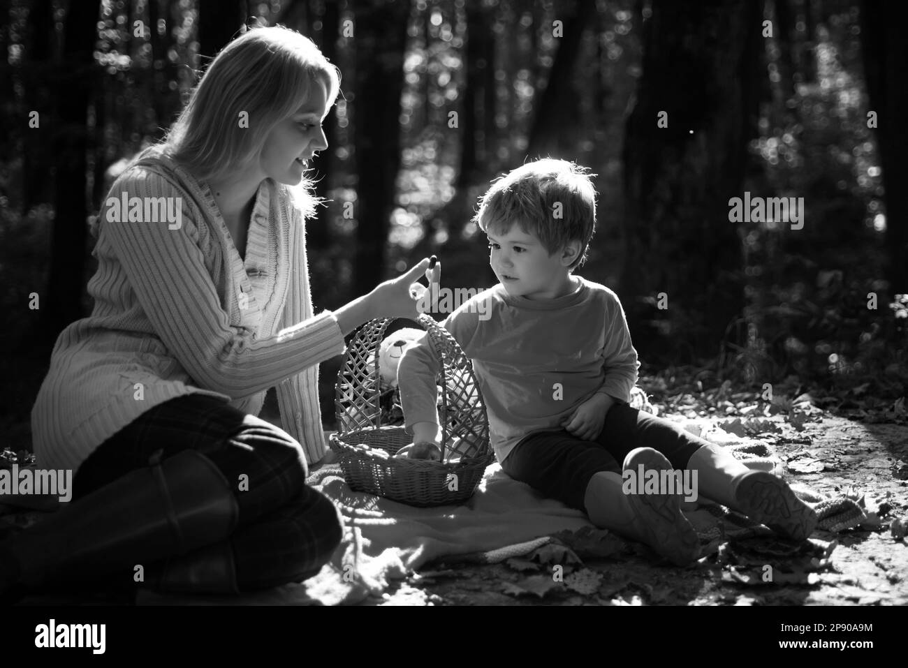 Junge Mutter, die ihrem kleinen Sohn beim Herbstpicknick eine süße Saisonberrie gibt. Mama und Kind sitzen auf der Picknickdecke und essen aus dem Picknickkorb Stockfoto