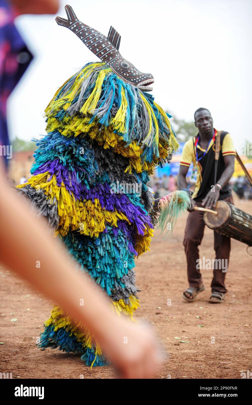 Eine farbenfrohe Fasermaske, die von Djembe-Musikern beim Festima Festival in Dedougou, Burkina Faso, begleitet wird Stockfoto