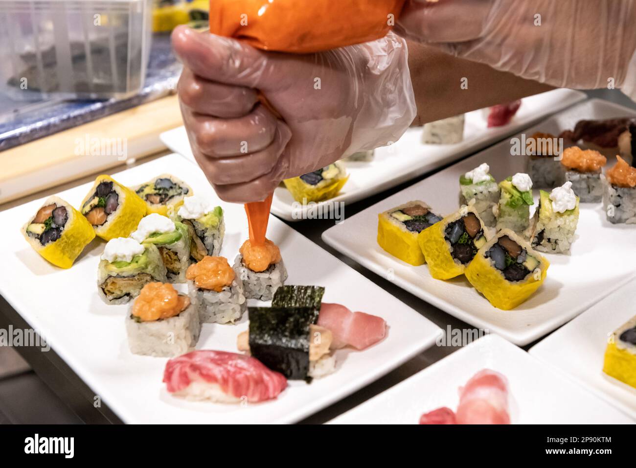 Ein unbekannter Koch in Handschuhen, der köstliches Sushi mit Sauce serviert, während er das Essen im Restaurant zubereitet Stockfoto