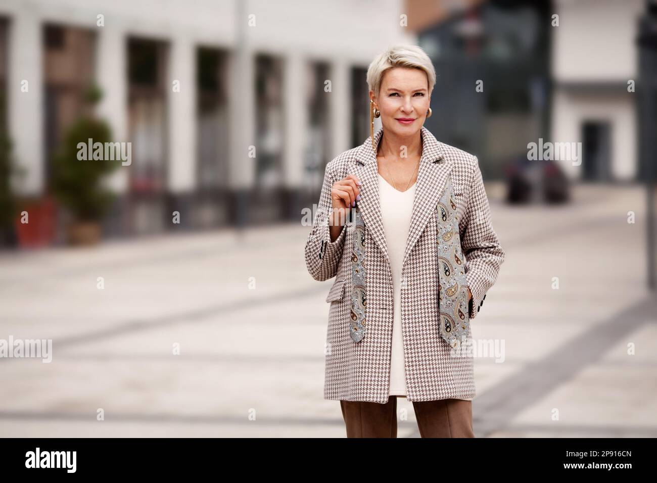 Porträt einer schönen, vertrauenswürdigen, reifen Geschäftsfrau mit blondem, kurzen Haarschnitt, modisch gekleidet in zweireihiger Jacke und Krawatte, auf der Straße Stockfoto