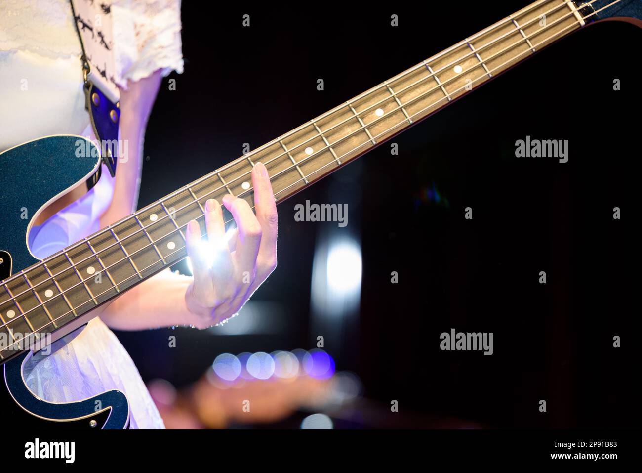 Musikerin in einem weißen Kleid, die elektrische Bassgitarre spielt. Nahaufnahme der Hand. Stockfoto