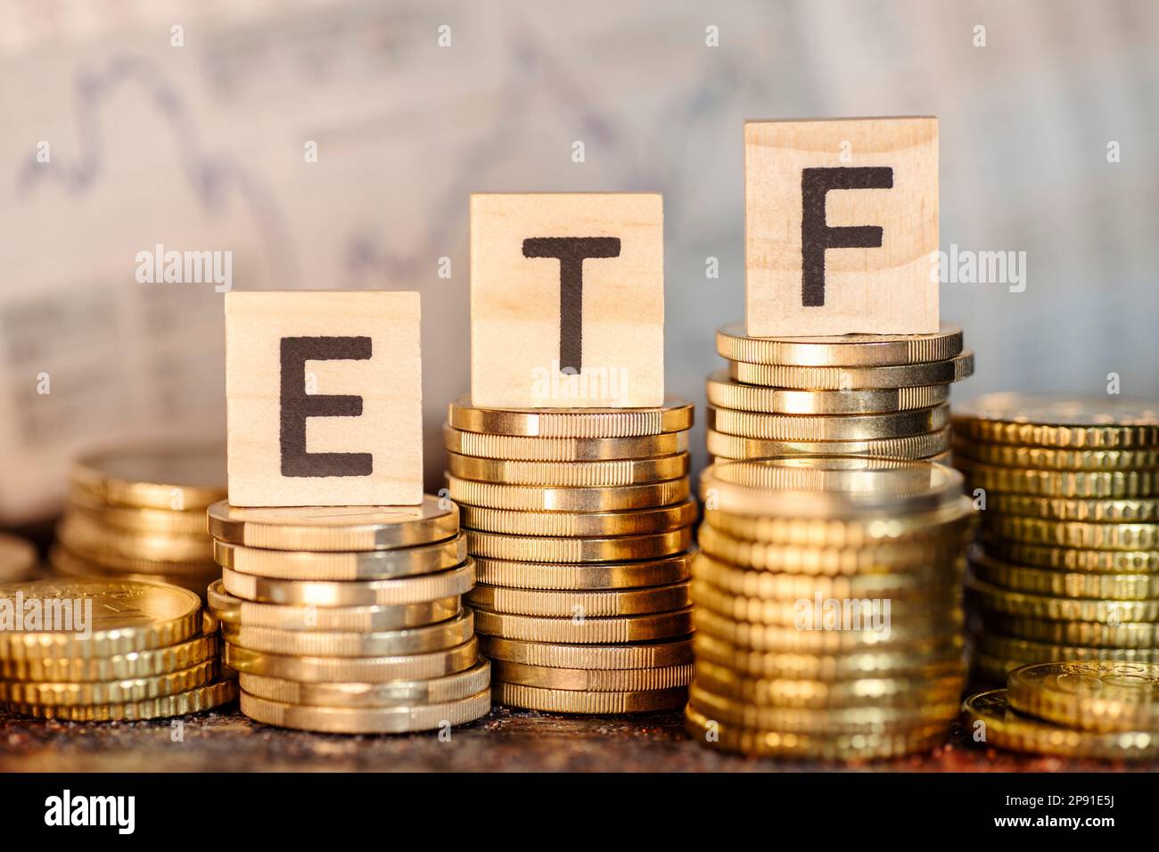 Mehrere Stapel mit Münzen und der Bezeichnung ETF und ein Diagramm mit Aktienkursen. Stockfoto