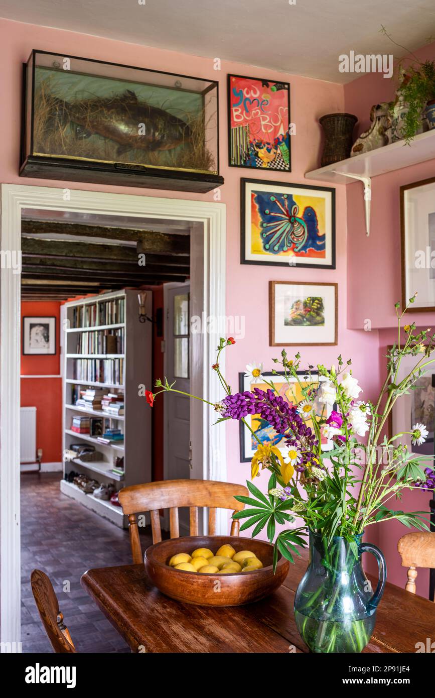 Schneiden Sie Blumen auf den Tisch in der rosafarbenen Küche mit gefüllten Fischen und Kunstwerken im Bauernhaus Tudor des 16. Jahrhunderts in Suffolk, Großbritannien. Stockfoto